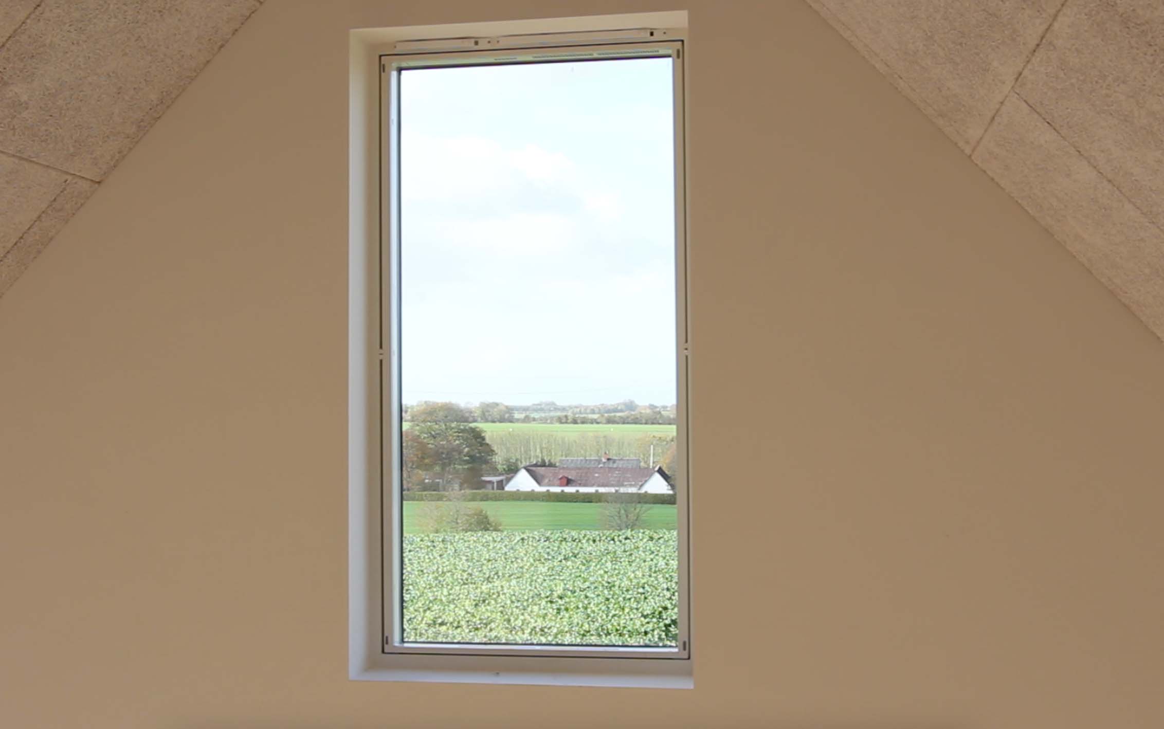 Her ses et ventilationsvindue under et loft beklædt med træbeton. Der er udsigt til en gård